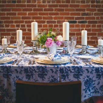 rectangle table with a blue floral patterned table cloth, napkins, plates, flowers, and candles