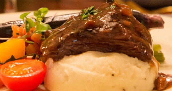 close up of plate with beef on top of mashed potatoes and vegetables