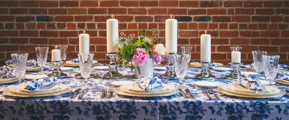rectangle table with a blue floral patterned table cloth, napkins, plates, flowers, and candles