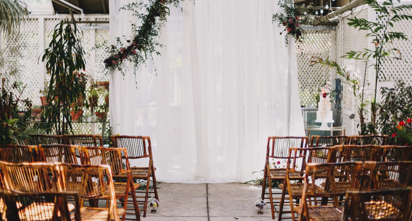 a wedding ceremony set up with brown wooden chairs, a white sheet, and vines