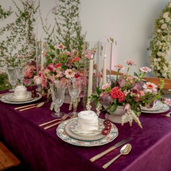 square table with maroon table cloth, intricate table setting, and floral arrangement