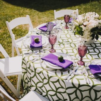 green patterned round table cloth with purple napkins and white chairs