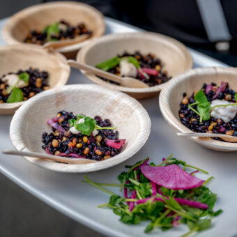 Five bowls of black bean salad with greens and a side of fresh salad on a white tray.
